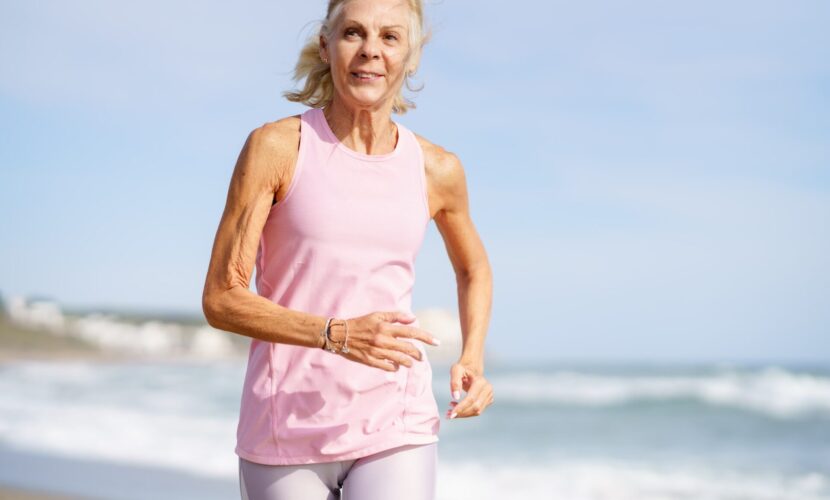Older female doing sport to keep fit. Mature woman running along the shore of the beach