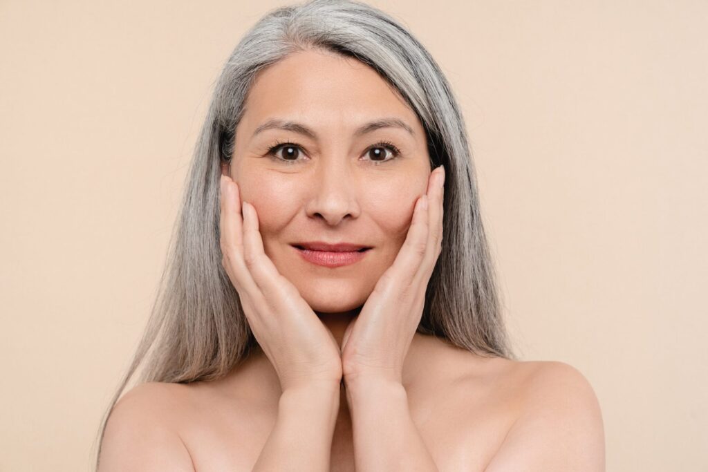 Woman touching her pure clear clean aging skin face looking at camera. Beauty and rejuvenation