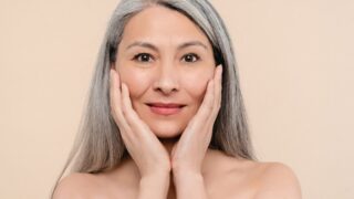 Woman touching her pure clear clean aging skin face looking at camera. Beauty and rejuvenation